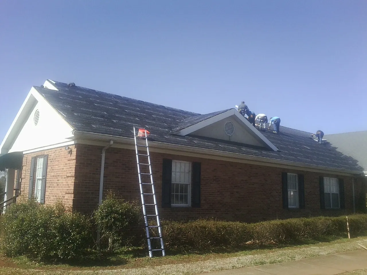 Crew tearing shingles off a brick ranch roof with a ladder set — Emergency Roof Repair work by our crew in Lurgan