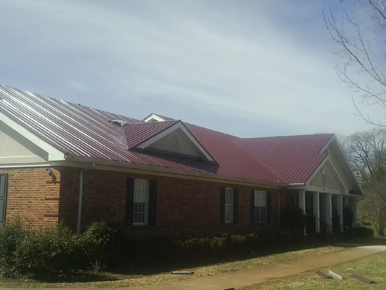 Red metal roof with gabled entries on a long brick building, from a Hail Damage Roof Repair job in Lurgan