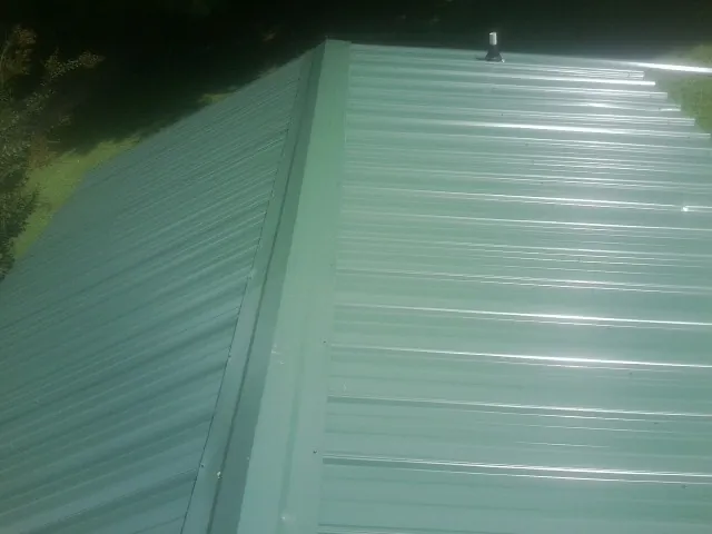 New green metal panels meeting at the ridge of a roof — Flat Roof Repair work by our crew in Lurgan
