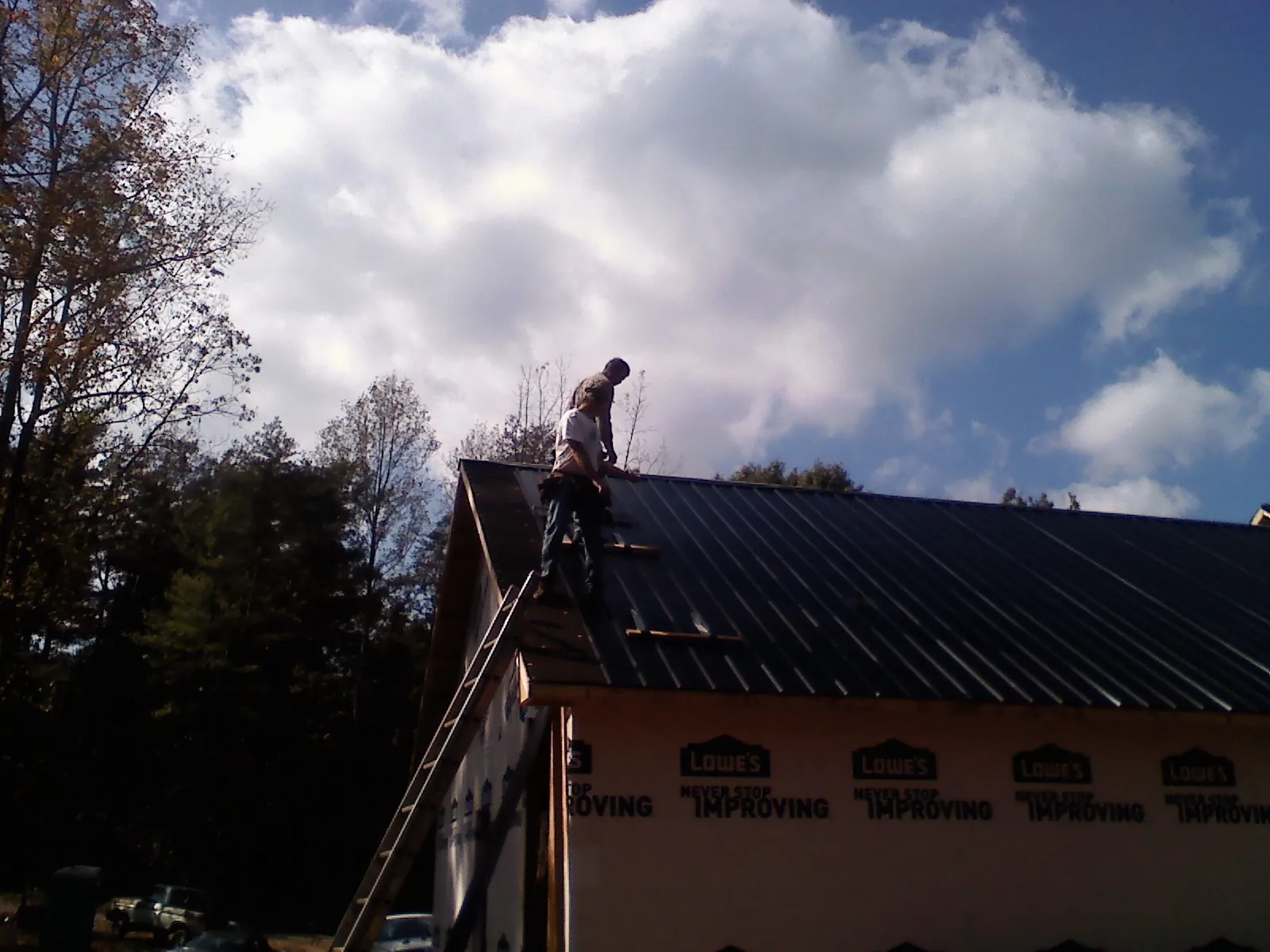 Roofer fastening dark metal panels high against a cloudy sky, from a Roof Inspection job in Lurgan