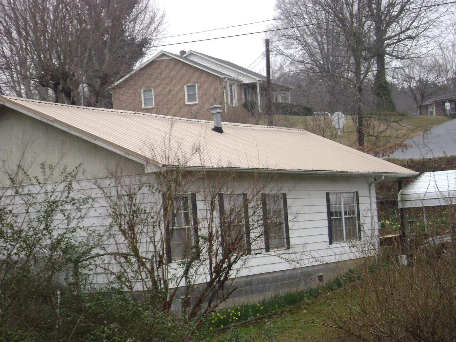 Tan metal roof on a white sided house set into a hillside — Commercial Roofing by Roofing Brothers in Lurgan